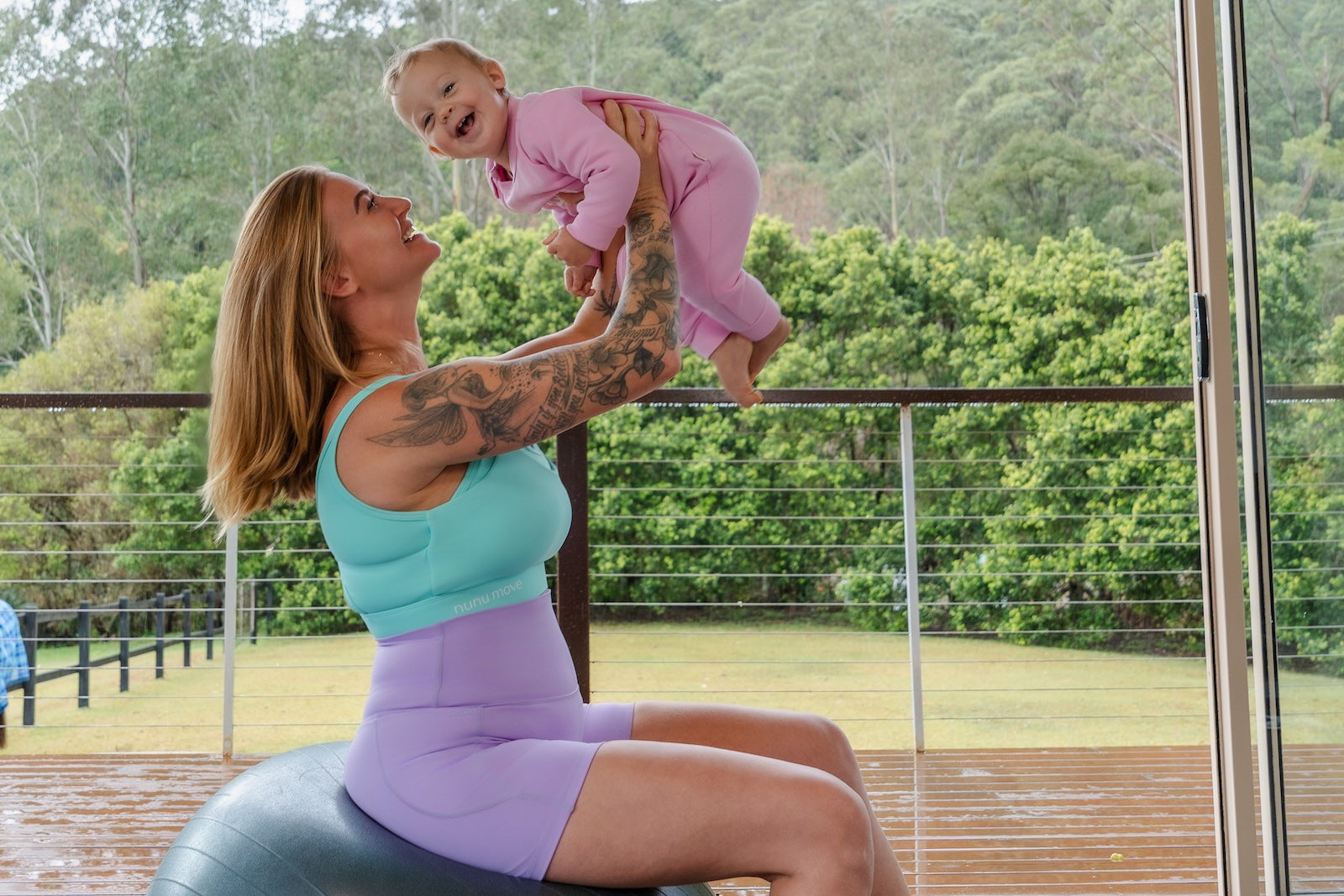 Woman exercising on a stability ball with a baby in her arms outdoors.