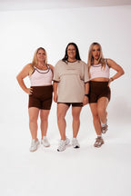 Three mums of different body types in Nunu Move activewear. Two in the Cherry Blossom Asta nursing bra with Espresso shorts, one in the Oat nursing tee with Espresso shorts. On a white studio background.