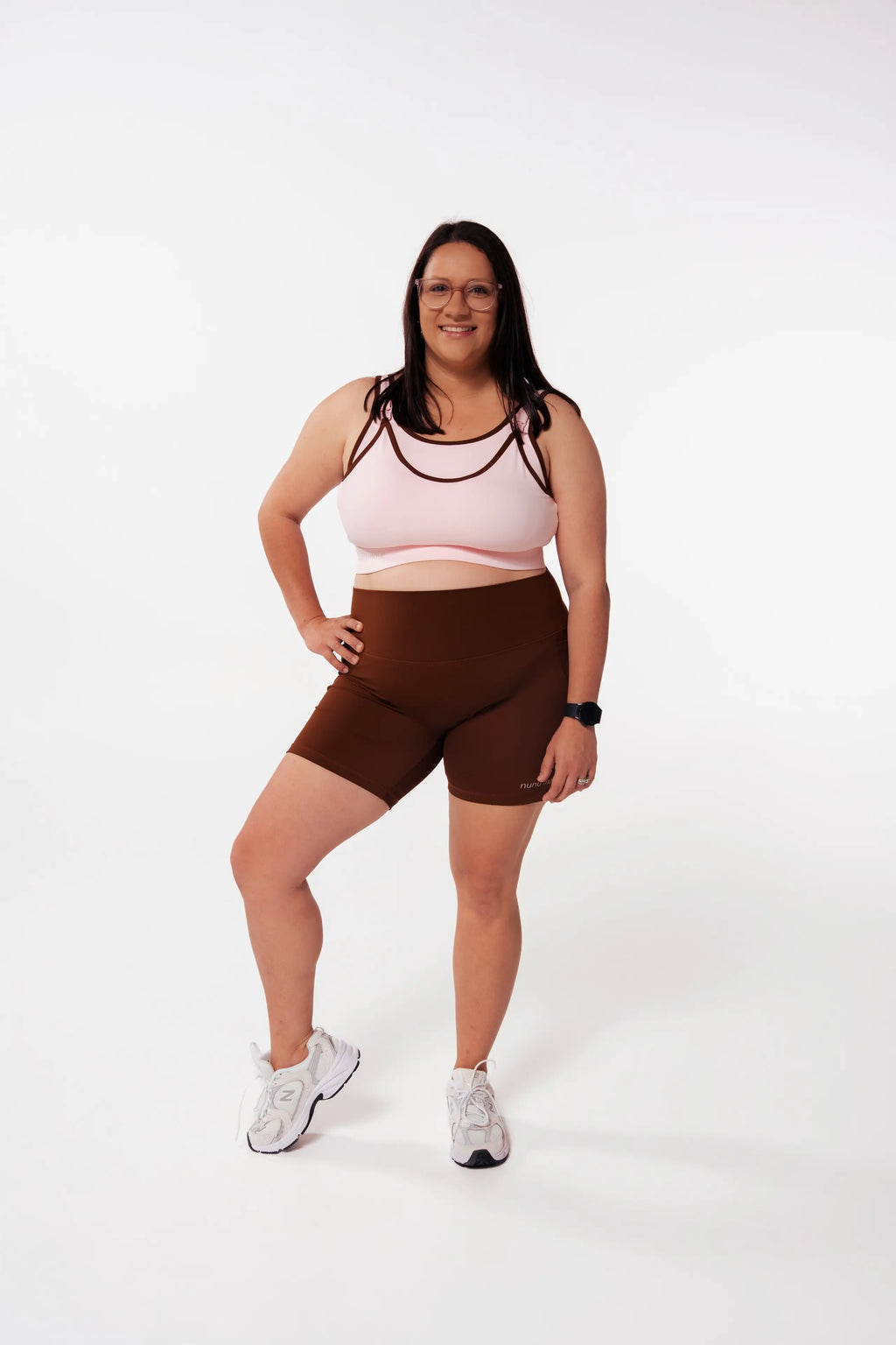 Woman wearing the Nunu Move Cherry Blossom Asta nursing bra with strappy detail and Espresso brown high-waisted bike shorts, front view on a white studio background.
