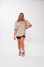 Woman wearing Nunu Move Espresso brown bike shorts styled with an oversized oat-coloured tee and sneakers, front view on a white studio background.